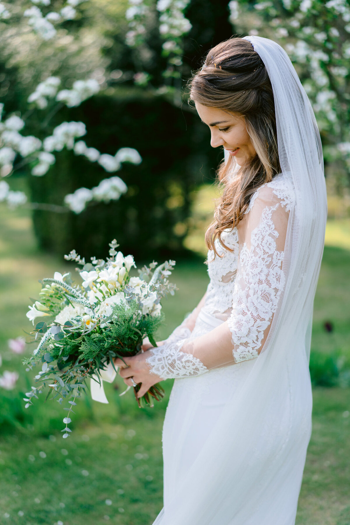 A fine art wedding photograph of the bride looking at her flowers in a field of blossom at Iscoyd Park