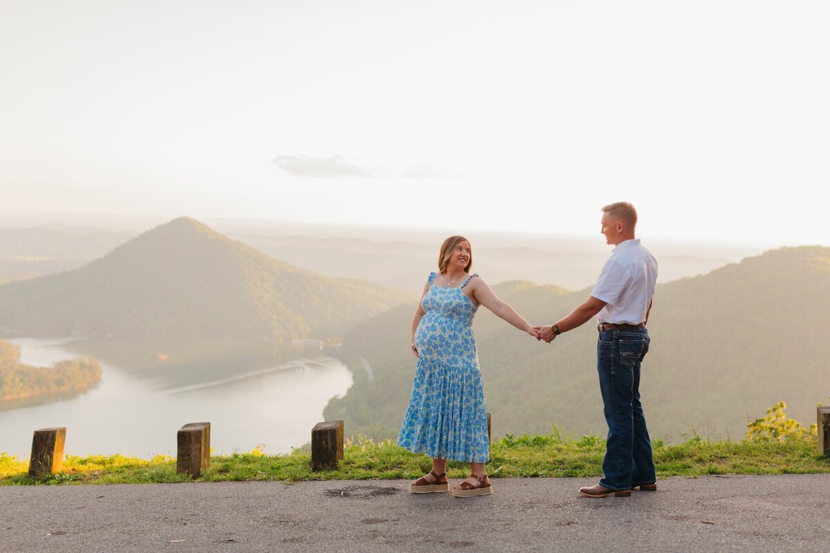a pregnant woman in a blue dress walking while holding hands with her husband