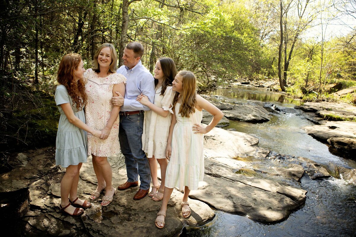 Three girls and their parents taking pictures by the creek, with the girls happily posing in the natural setting