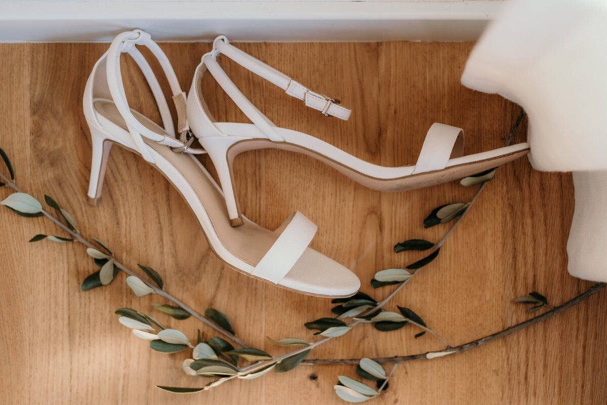 Die weißen Sandalen der Braut liegen seitlich auf dem Boden umrahmt von Olivenzweigen.