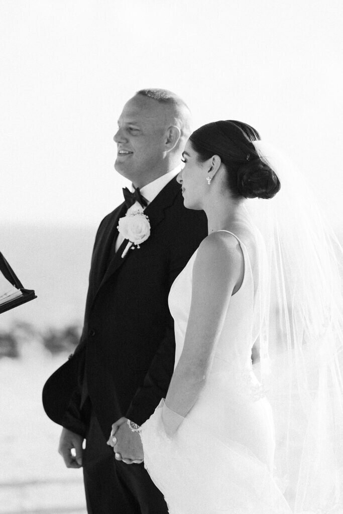 A timeless black-and-white moment as the bride and groom stand together, holding hands and listening to their officiant during their beachfront wedding ceremony. Captured by Claudia Amalia Photography, a Florida Keys wedding photographer specializing in destination wedding photography.