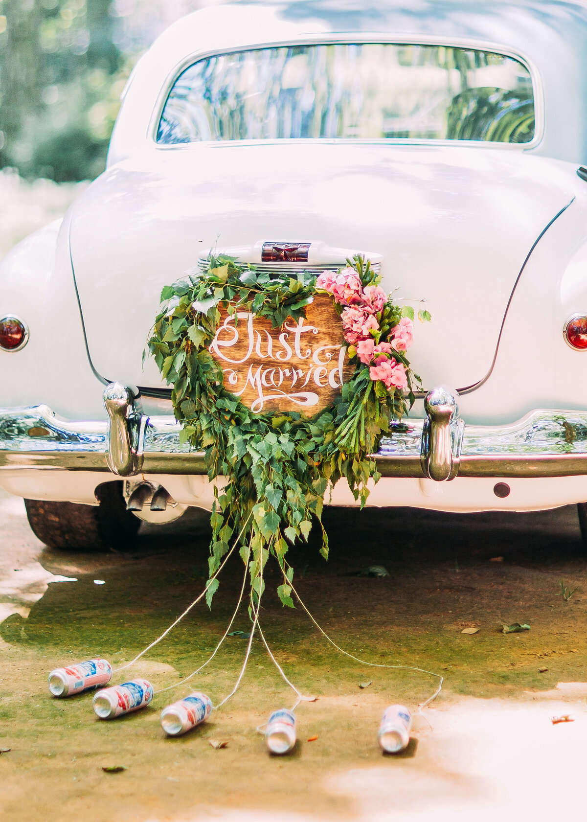 Vintage white wedding car with a just married sign surrounded by flowers with cans attached.