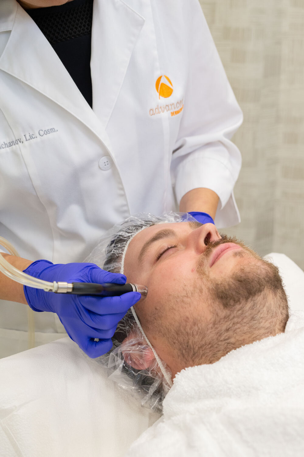 A man is getting a facial treatment from a woman wearing blue gloves