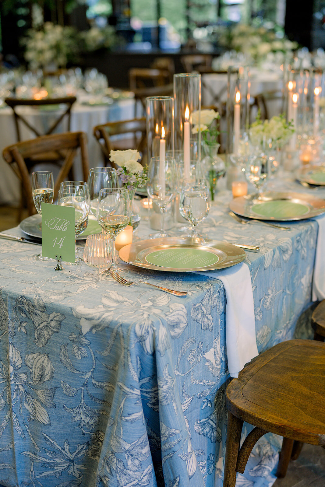 Long reception table with white and soft blue florals, tapered candles, and layered place settings.