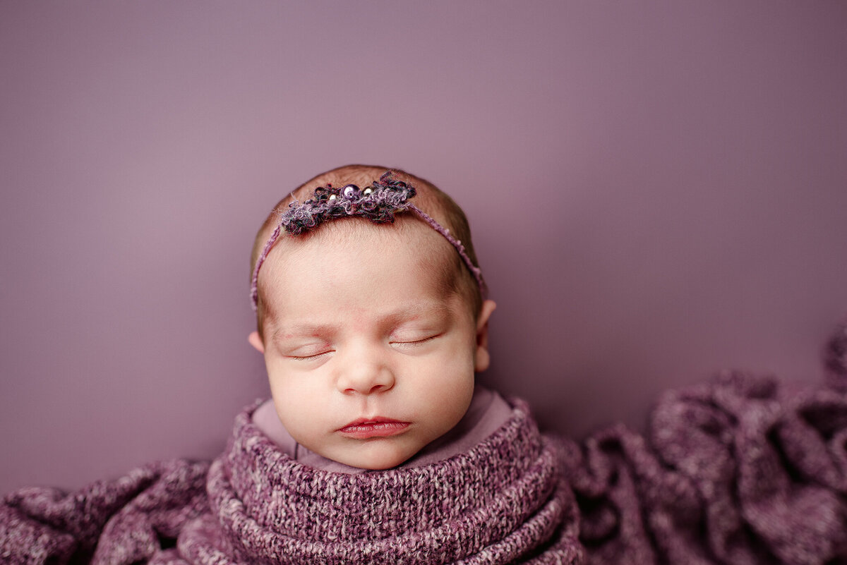 Studio newborn portrait of baby girl wrapped on purple backdrop in St. Augustine, FL.