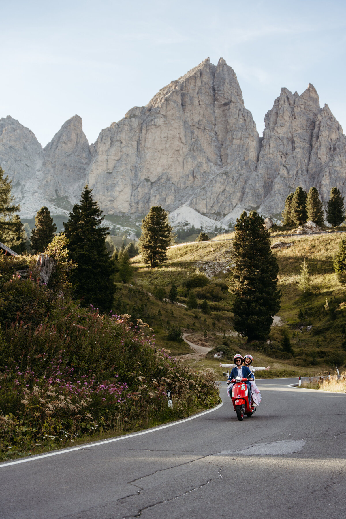 Bride and groom riding red Vespa through Dolomites mountain road