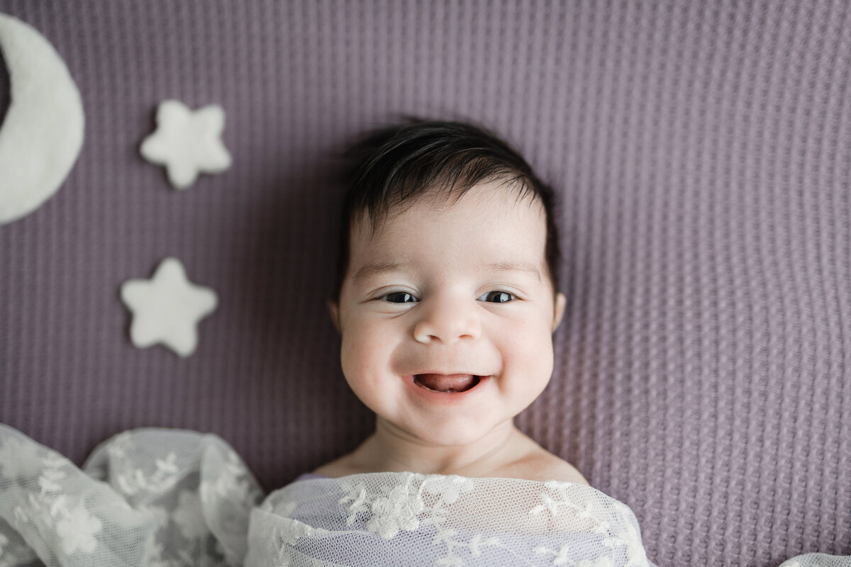 smiling newborn on a purple backdrop next to moon and stars prop