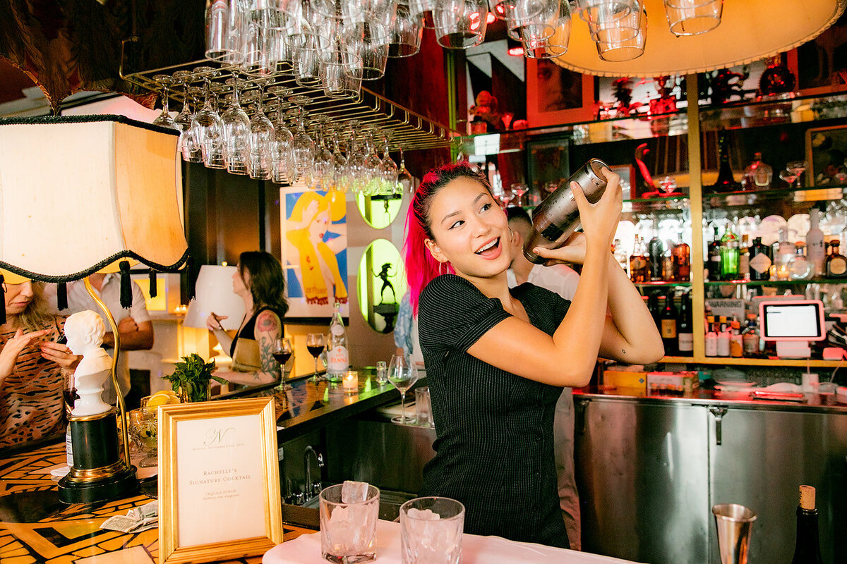 Smiling bartender shakes a cocktail behind the bar.