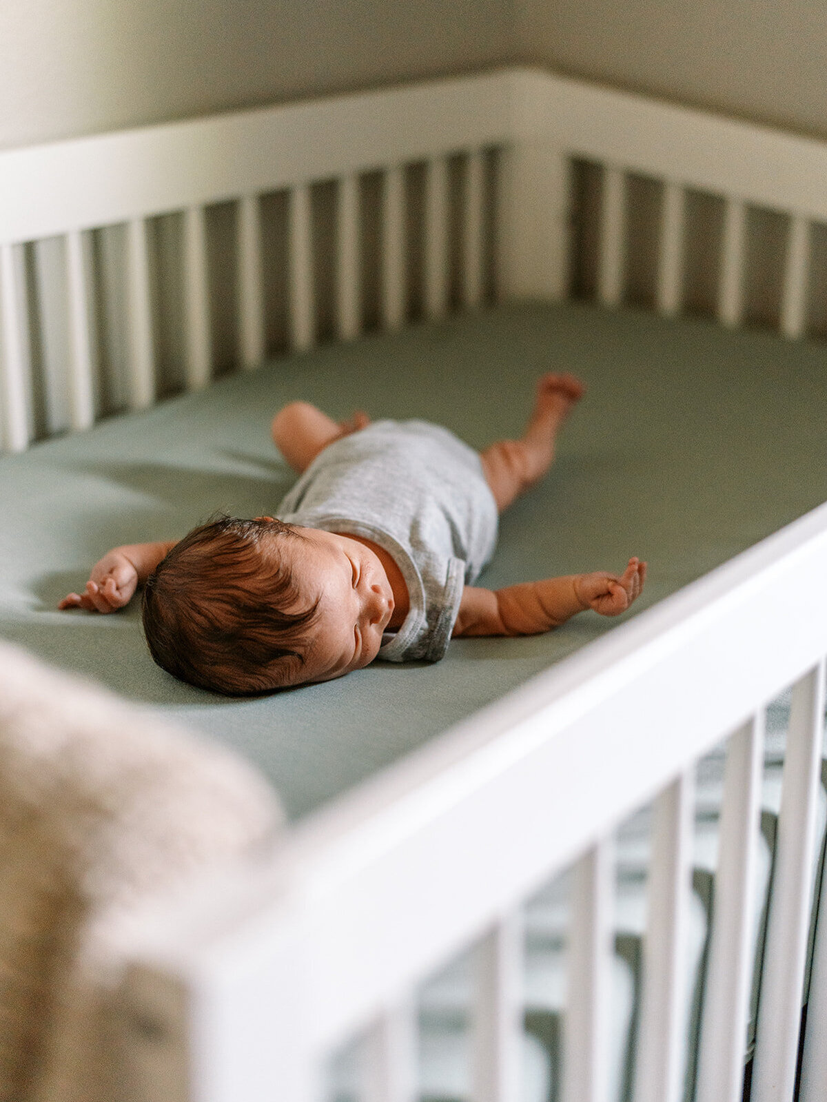 A baby laying on their back in a crib during a newborn photo shoot.