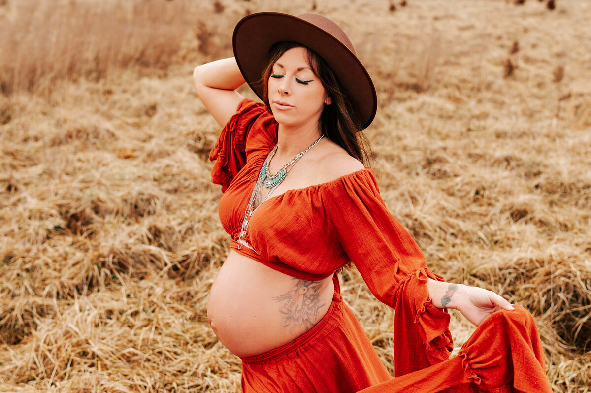 maternity photo in Springfield MO of pregnant mom taking a deep breath standing in a field holding her hat