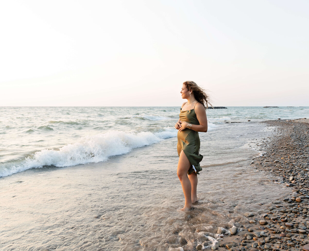 Senior photo of a girl in a green dressing looking off over the water on Lake Erie