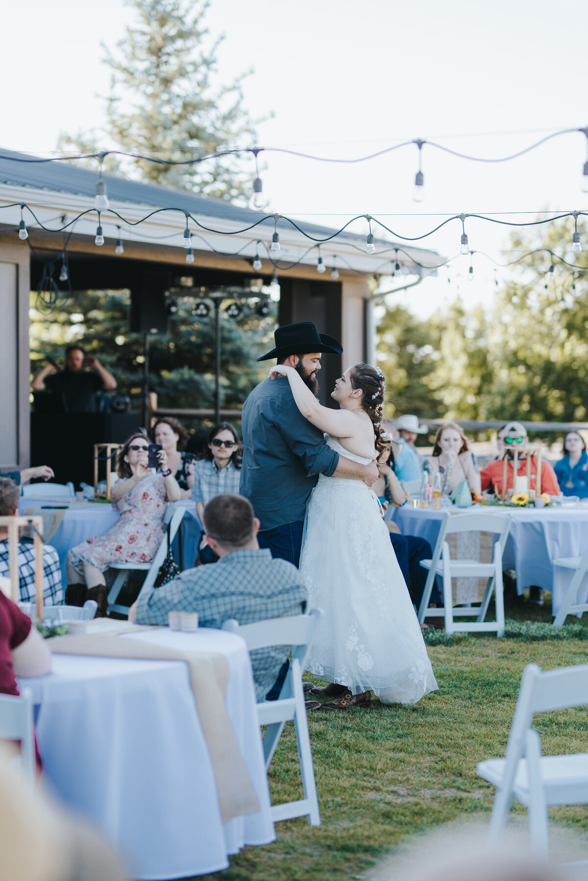 First dance outdoors under string lights, guests at tables