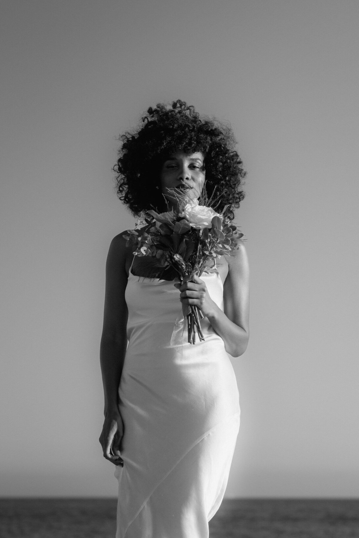Black and white photography of the bride standing straight, holding her bouquet in front of her.