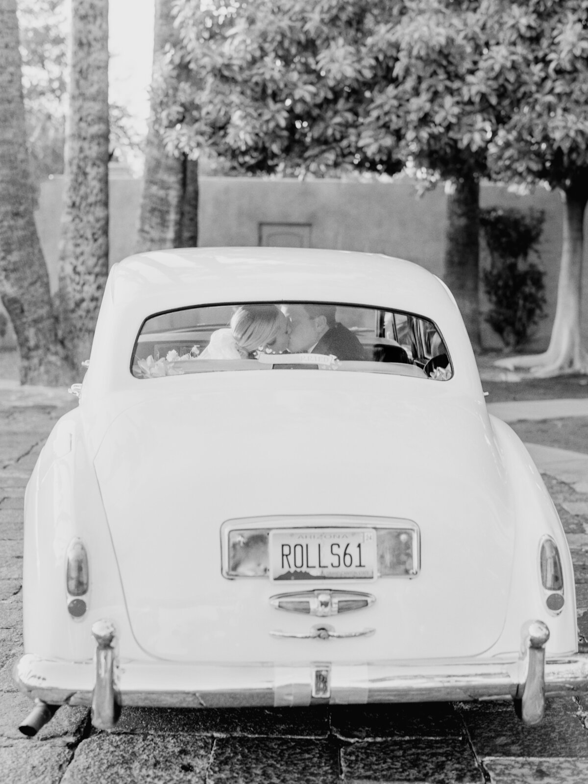 The bride and groom steal a kiss in the back of a vintage Rolls-Royce, marking a picture-perfect and timeless wedding getaway moment.