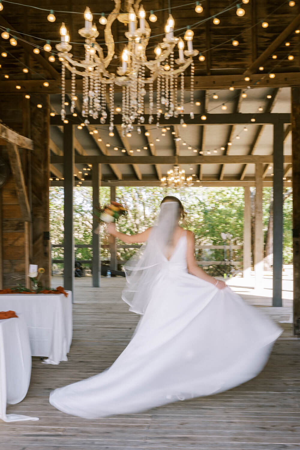 bride-twirling-under-chandelier-in-barn