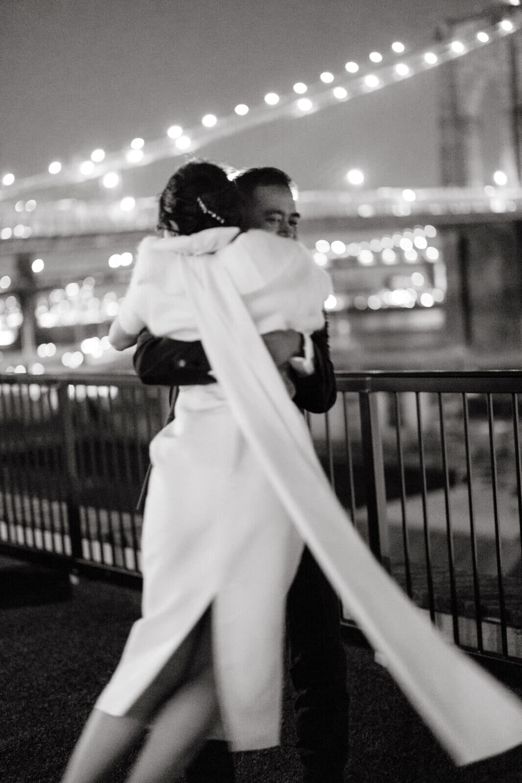 Back view of the bride while hugging the groom on a veranda overlooking the Brooklyn Bridge.