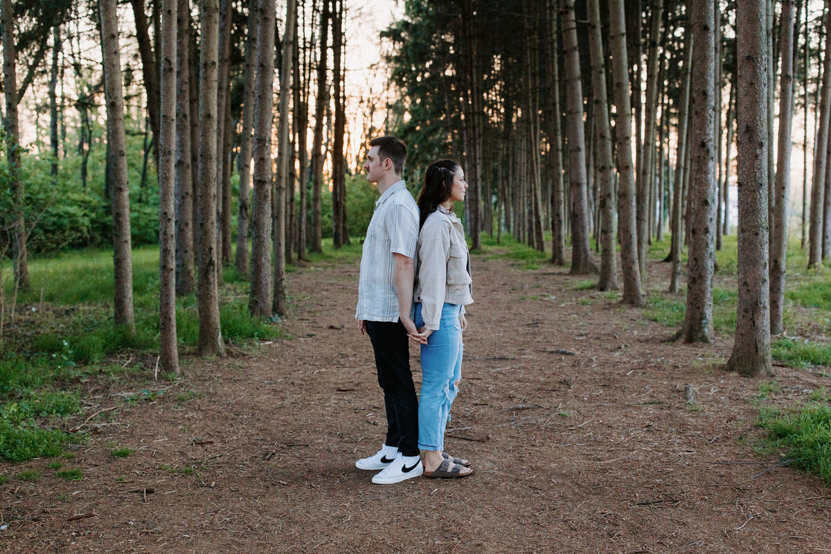 couple standing back to back holding hands on a path in the woods
