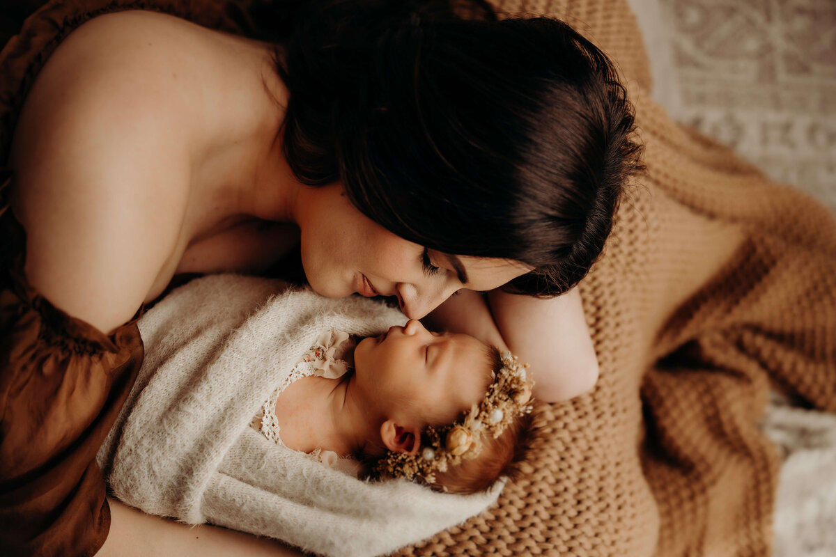 mom lays on bed nuzzling nose of newborn baby girl
