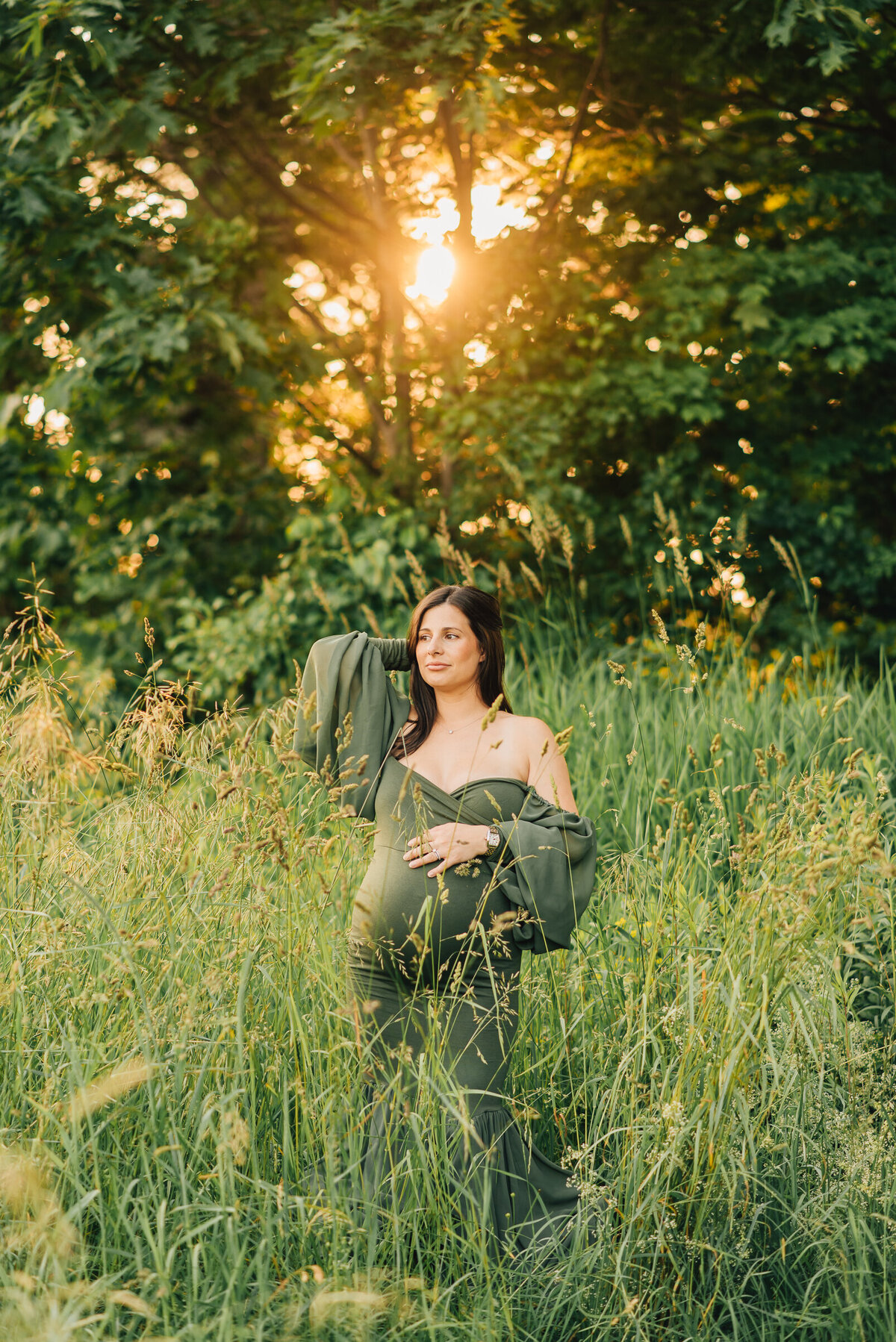A pregnant mom in a field of green grass, wearing a green dress and looking off camera