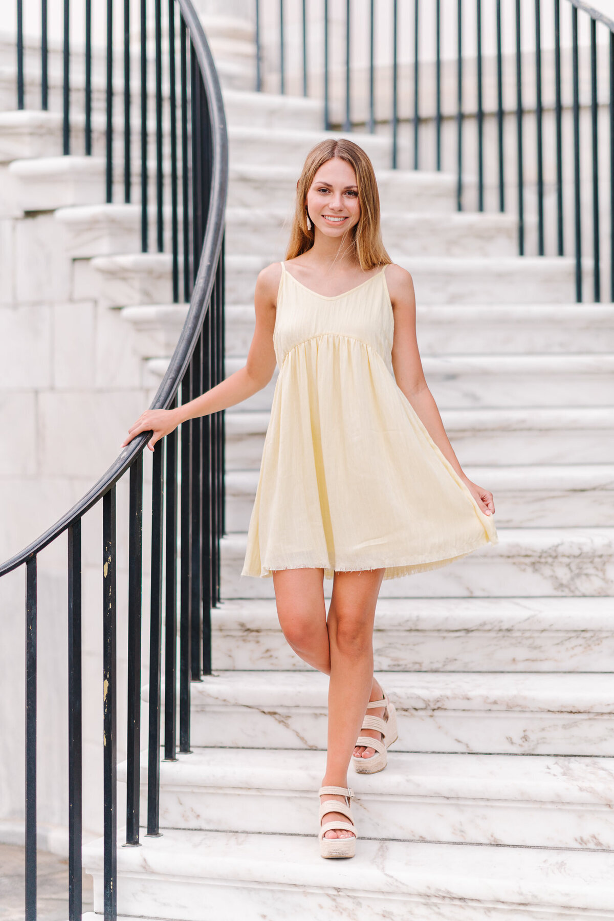 Senior girl in white dress posing on stone steps in Charleston’s historic district