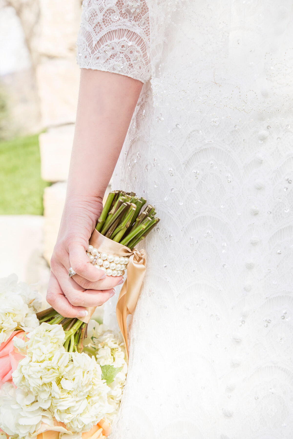 bright wedding day detail of pearls around bridal bouquet held by bride in a lace and beaded dress