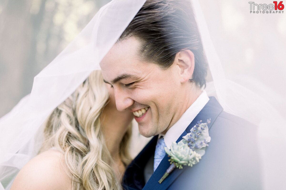Bride whispers in her Groom's ear causing him to smile while under her veil