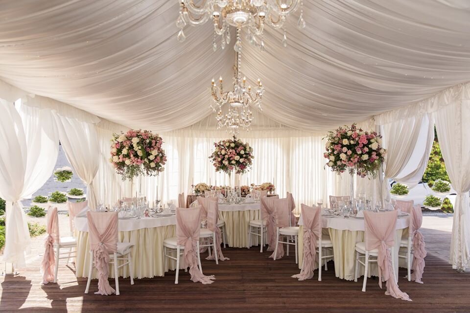 Round tables decorated with  tall fresh flower arrangements in an open marquee