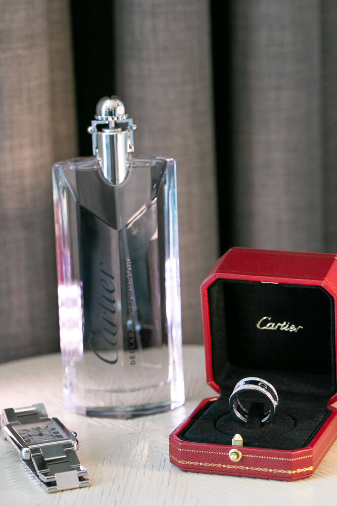 A wedding ring in a box with a watch and cologne next to it