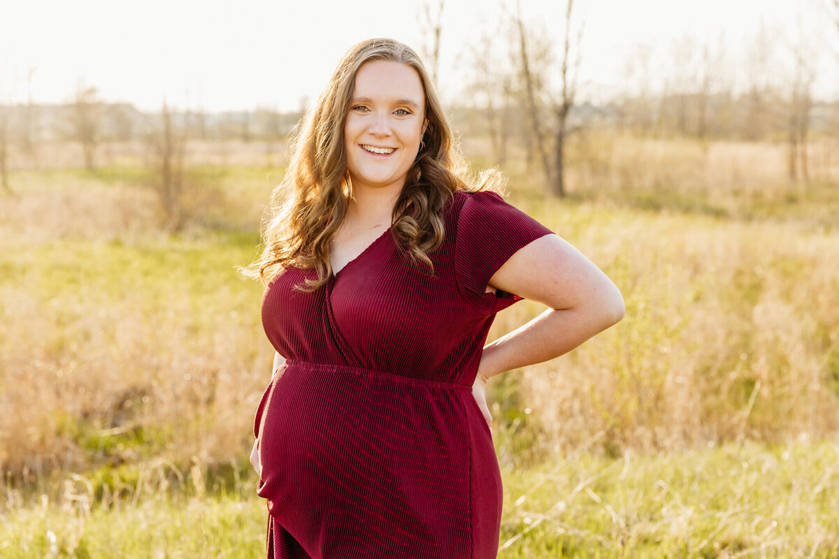 brown haired pregnant woman smiling in a grassy field near Green Bay, WI