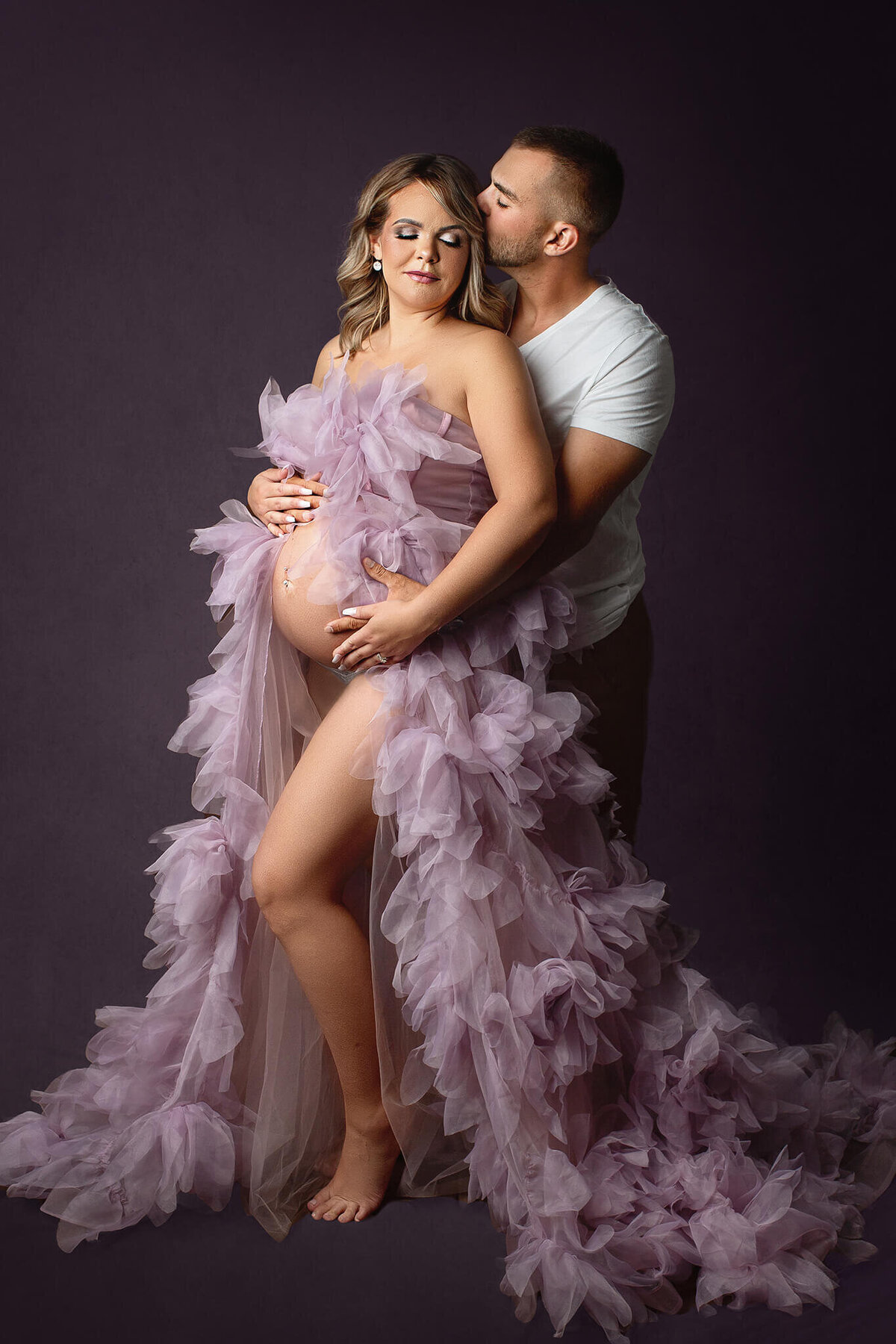 expecting father kisses mama on the side of the head while posing for maternity photos
