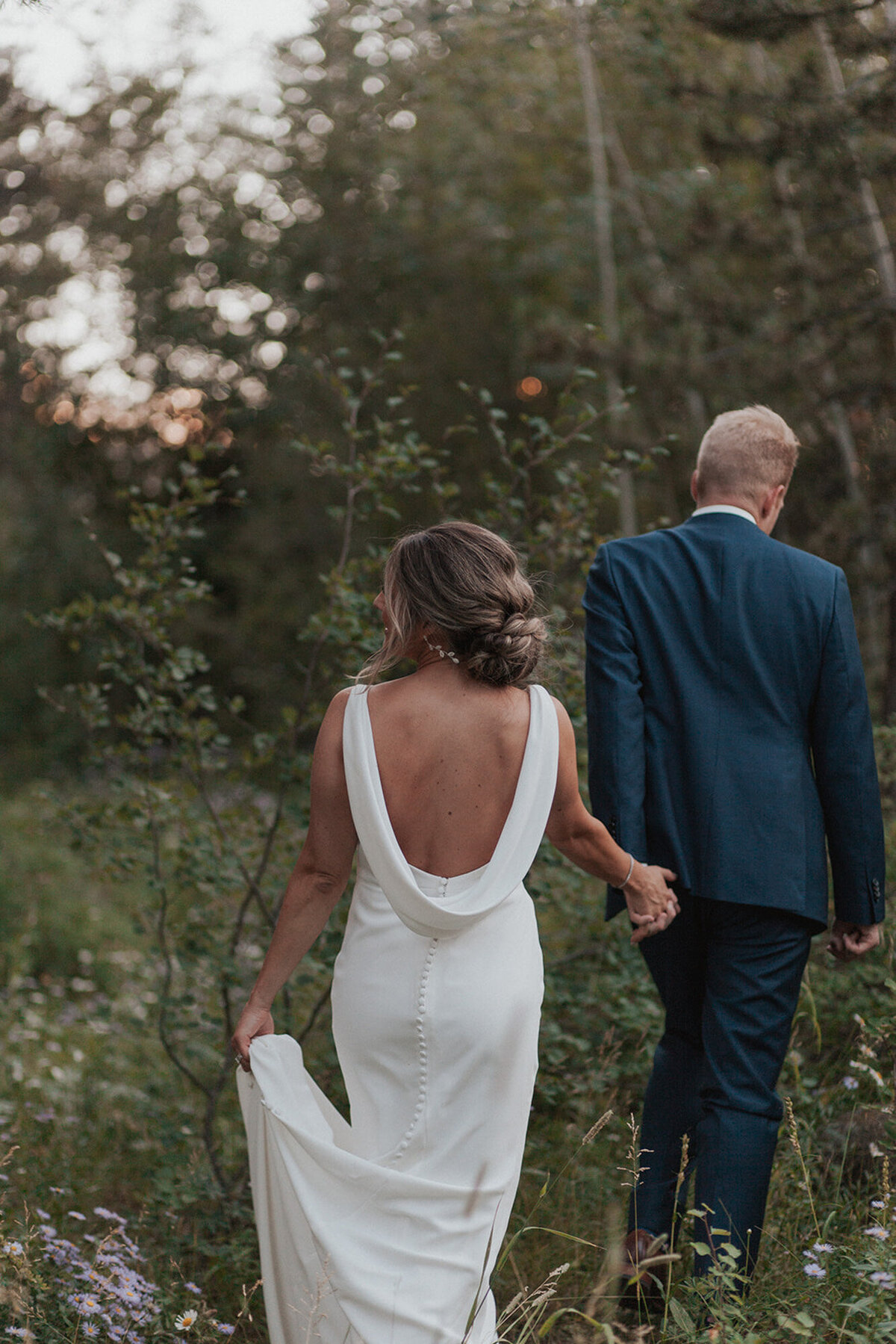 Alana and Ryan walking together while holding each other's hand through the field f the grass and flowers