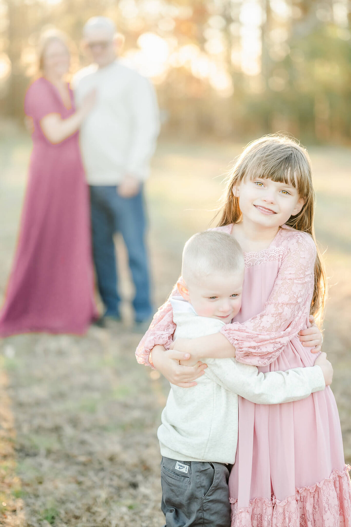 A brother and sister hug while standing in front of their mom and dad during a family session in Virginia Beach.