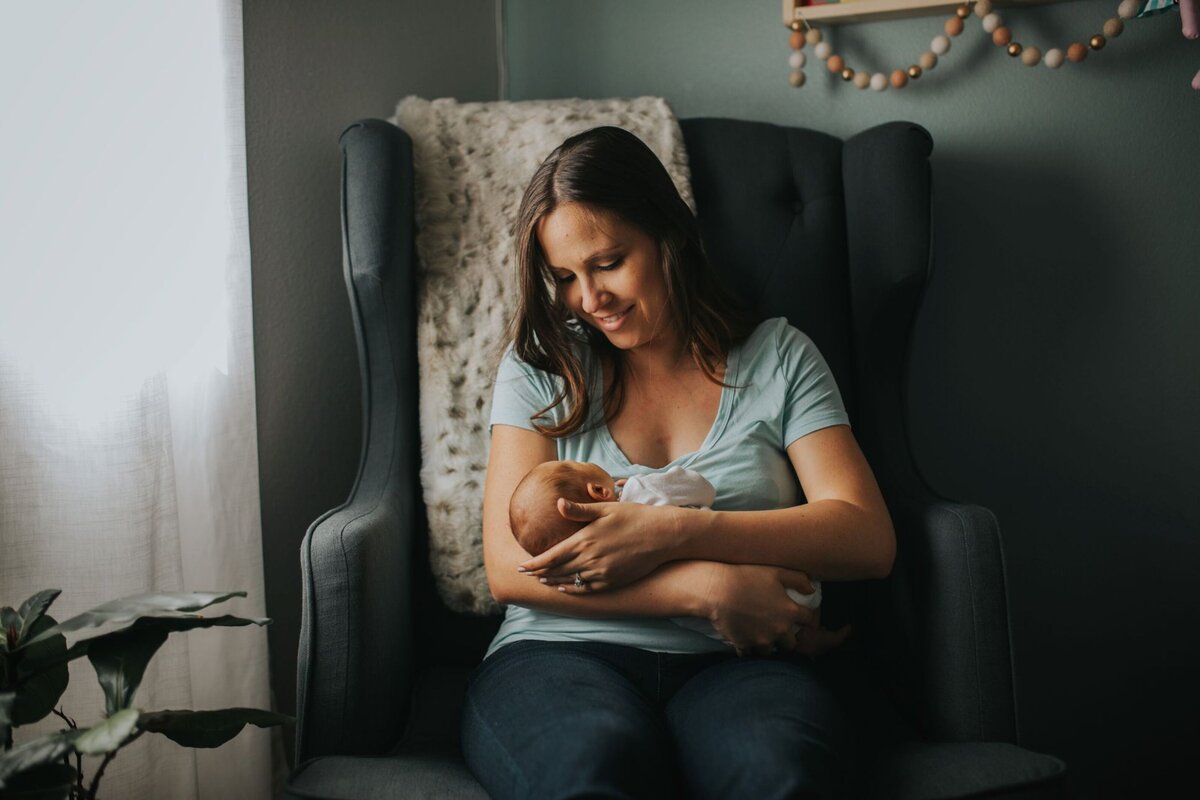 mother holding newborn in chair in dark nursery