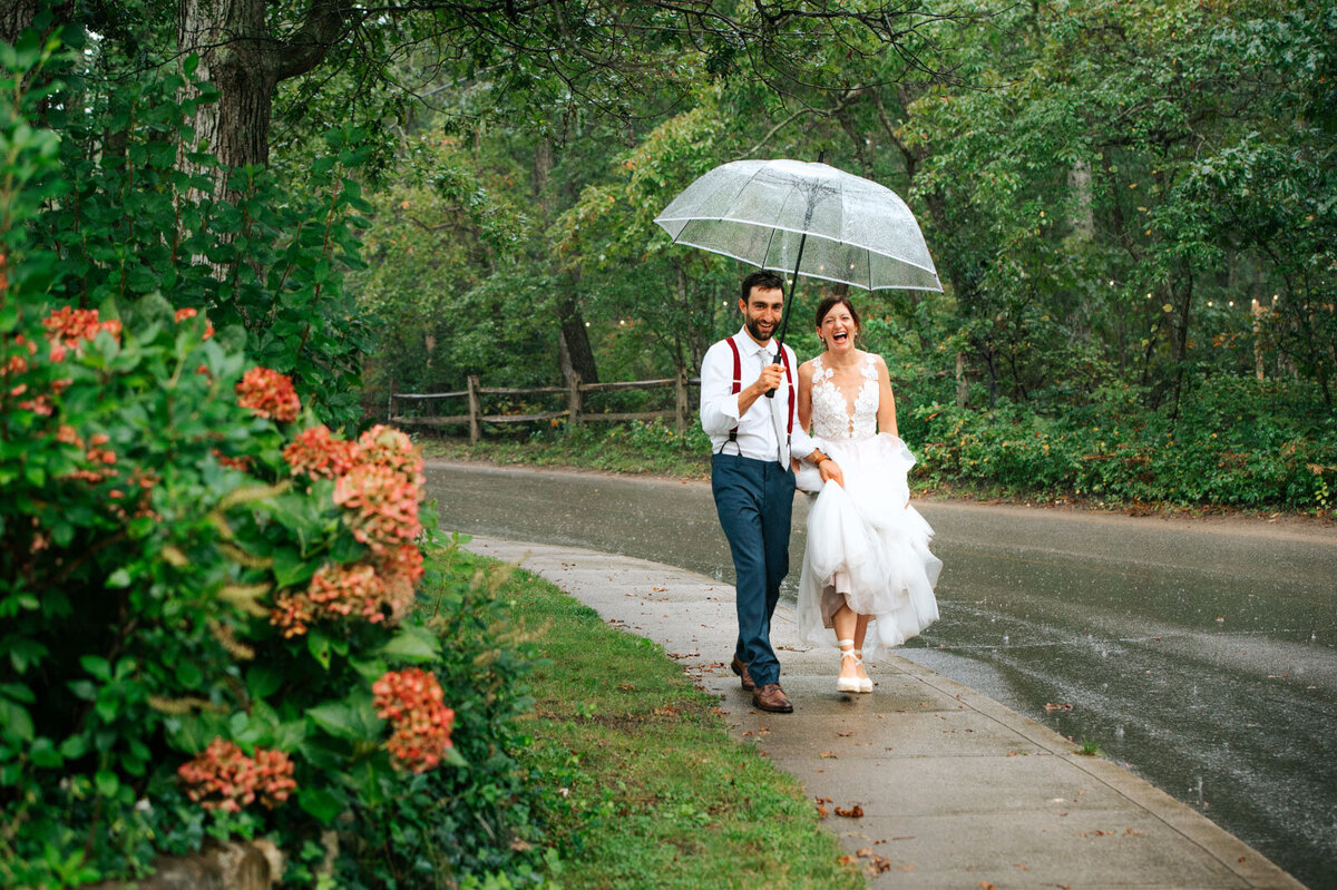 bride and groom walk in the rain laughing with umbrella at martha's vineyard wedding