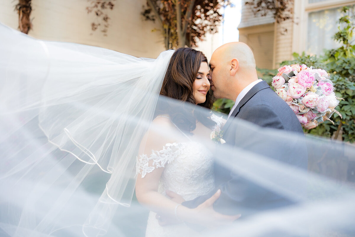 Bride and groom press faces to each other while the bride's long veil wraps around her body and into the camera lens. Creatively captured by sacramento wedding photography studio philippe studio pro.