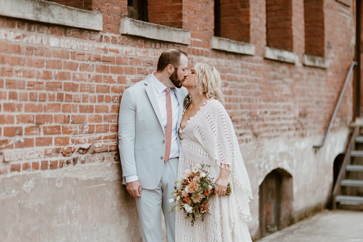 Newlyweds lean on a brick wall in an alley kissing