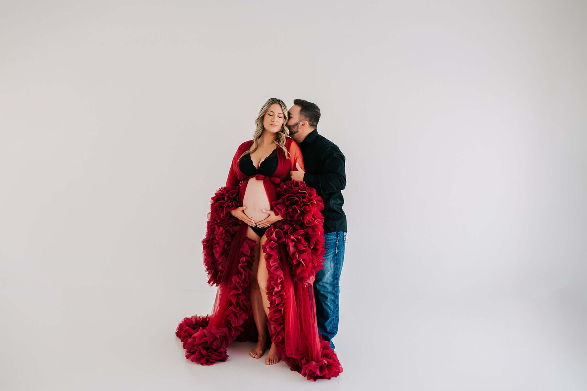 pregnant couple cuddling in white studio geting maternity pictures in Joplin MO
