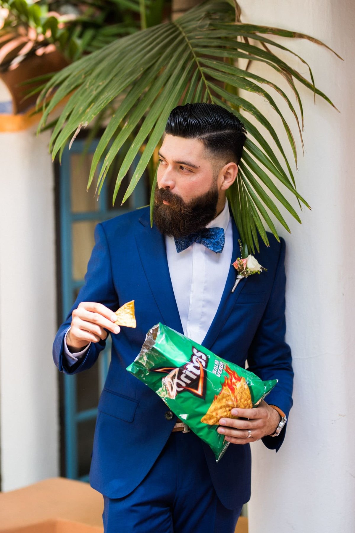 Groom leans against a wall eating Doritos Chips before the ceremony