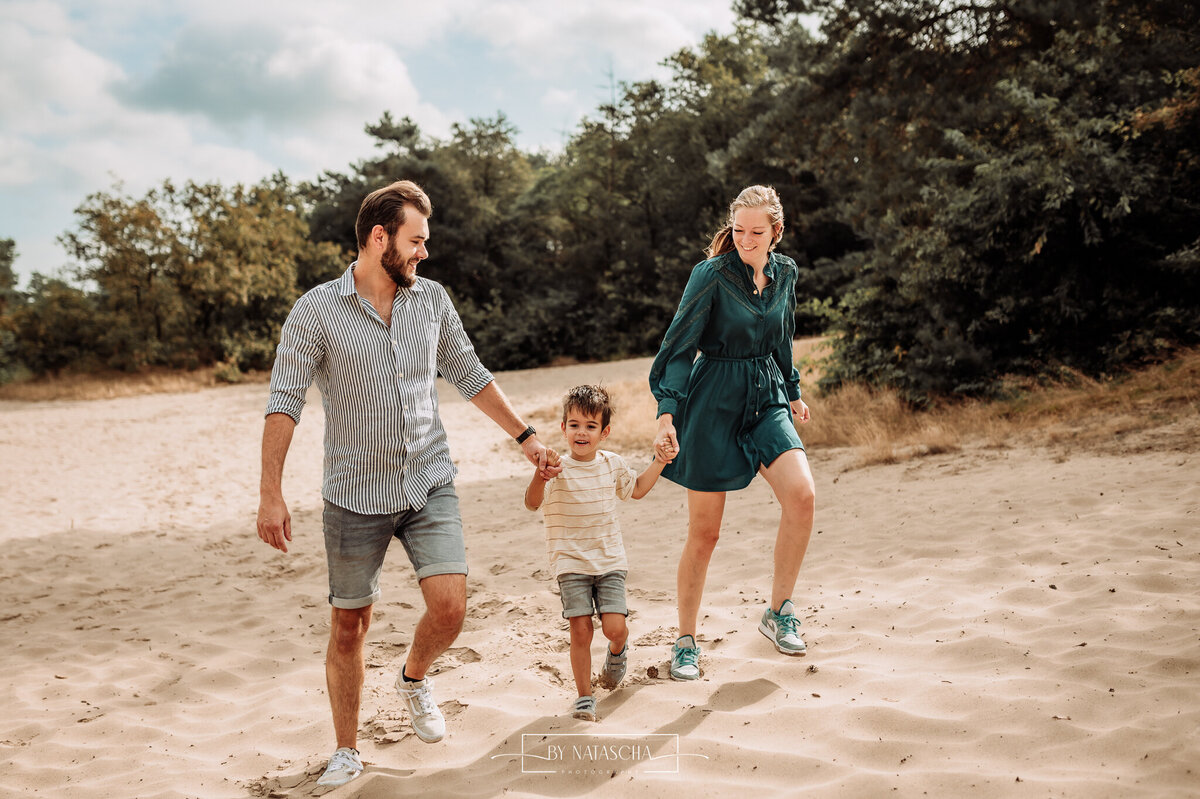 Papa, mama en zoon in het midden lopen hand in hand door de duinen bij Bedafse Bergen in Uden