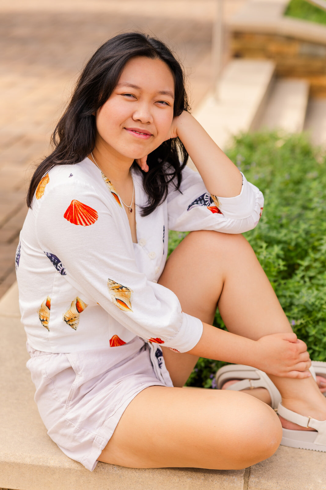 senior girl sitting on the ground one knee up resting her head on her elbow looking sideway at the camera during portraits photo session