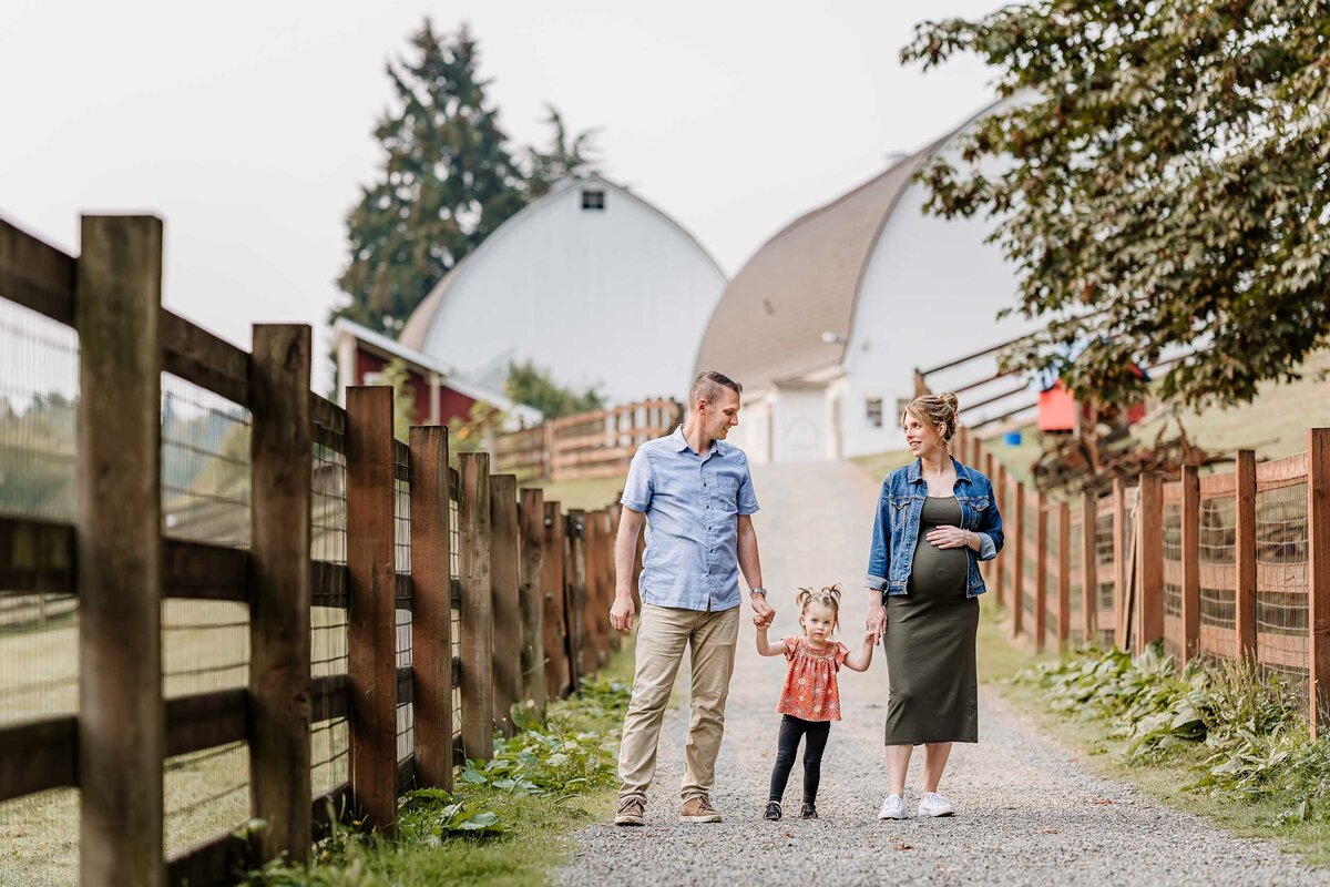 Family of three, including a pregnant mama, walking hand in hand at Kelsey Creek Farm in Bellevue during a serene maternity session.