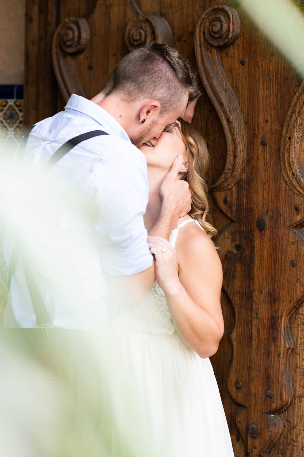 A wedding couple about to kiss while standing next to a wooden door.