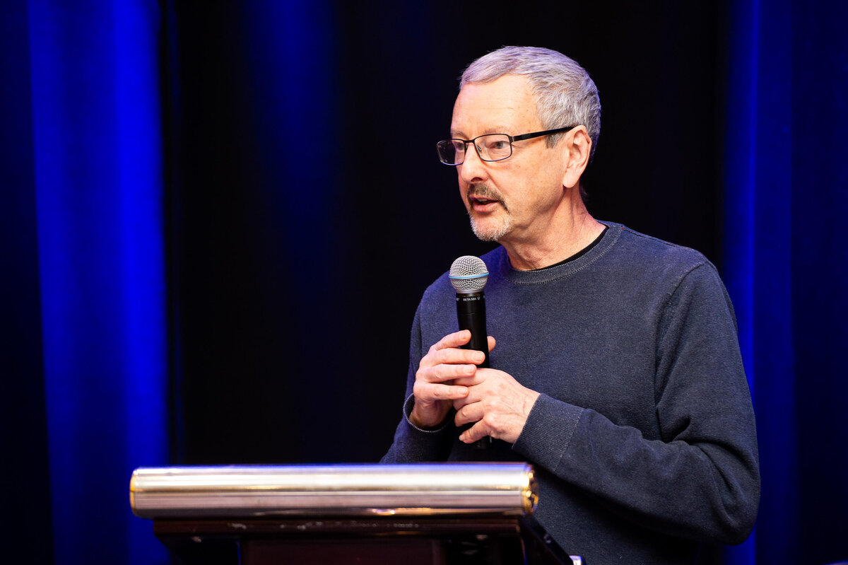 Ottawa event photography showing a man in a grey sweater speaking into a microphone during a corporate conference.  Captured by JEMMAN Photography COMMERCIAL