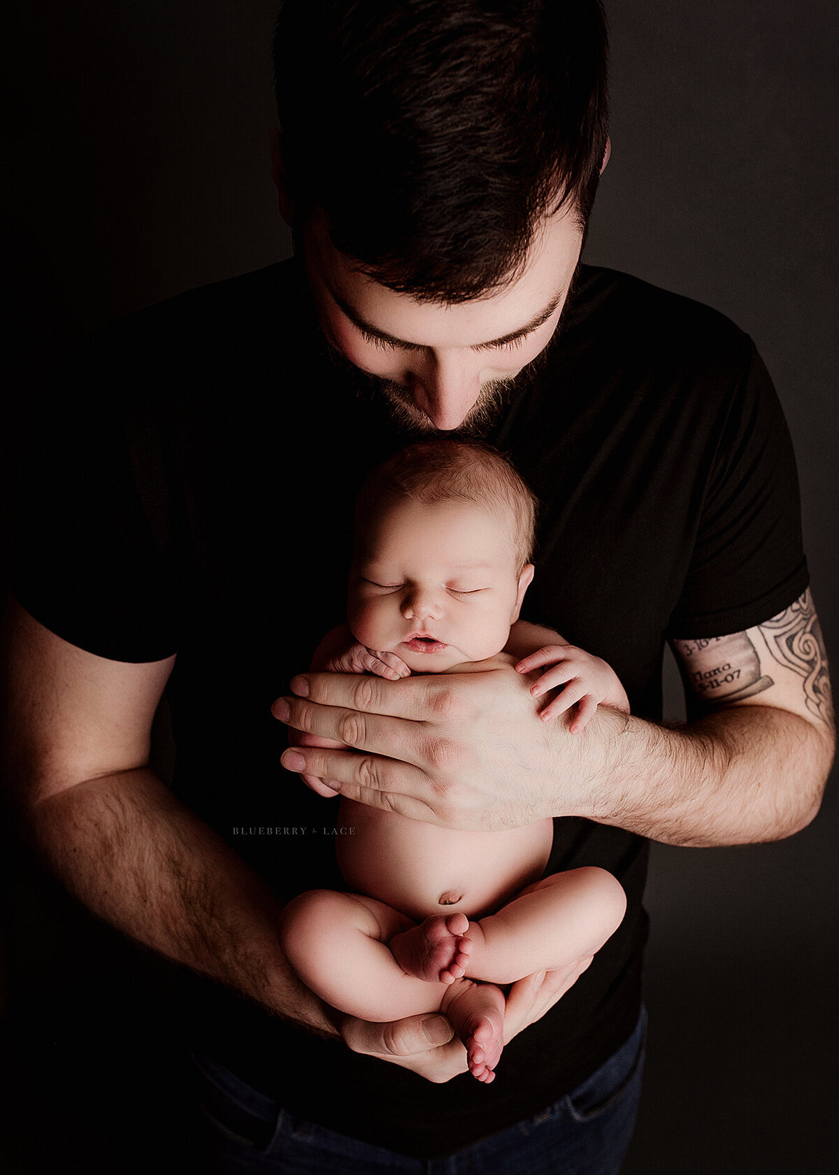 daddy holding his baby newborn boy so perfectly in his hands wearing black