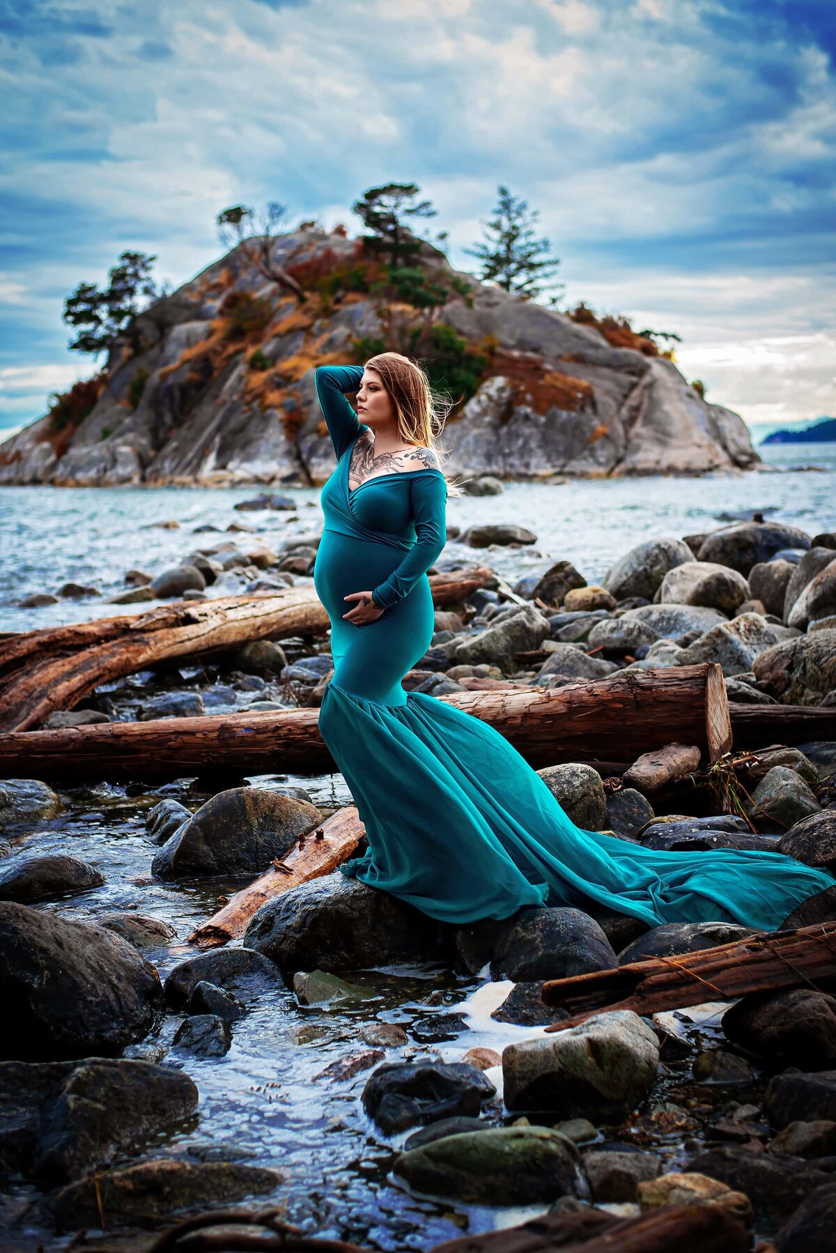 Pregnant mother in teal chiffon dress on a rocky beach.