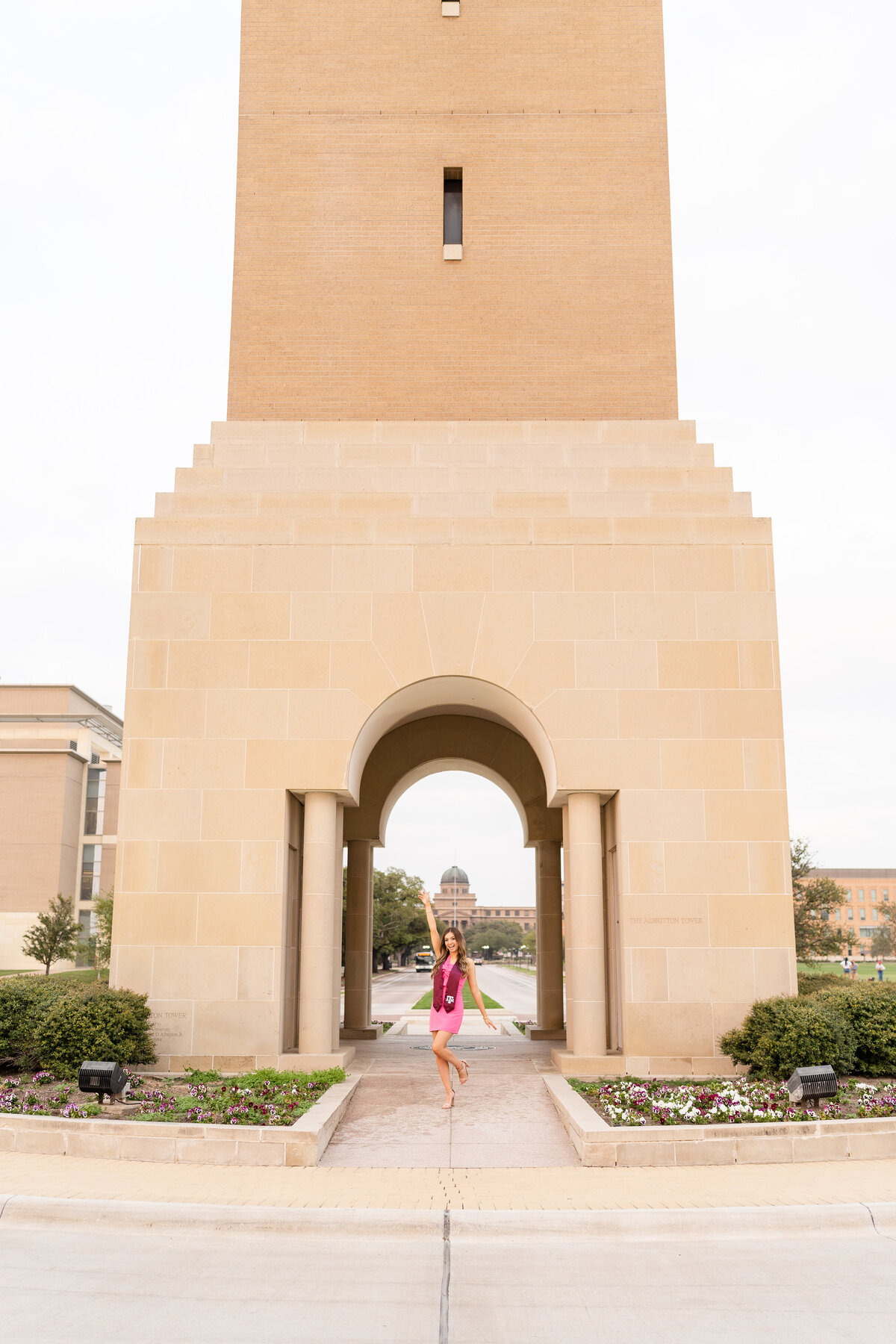 Texas A&M Senior girl at Bell Tower celebrating in pink dress and maroon stole