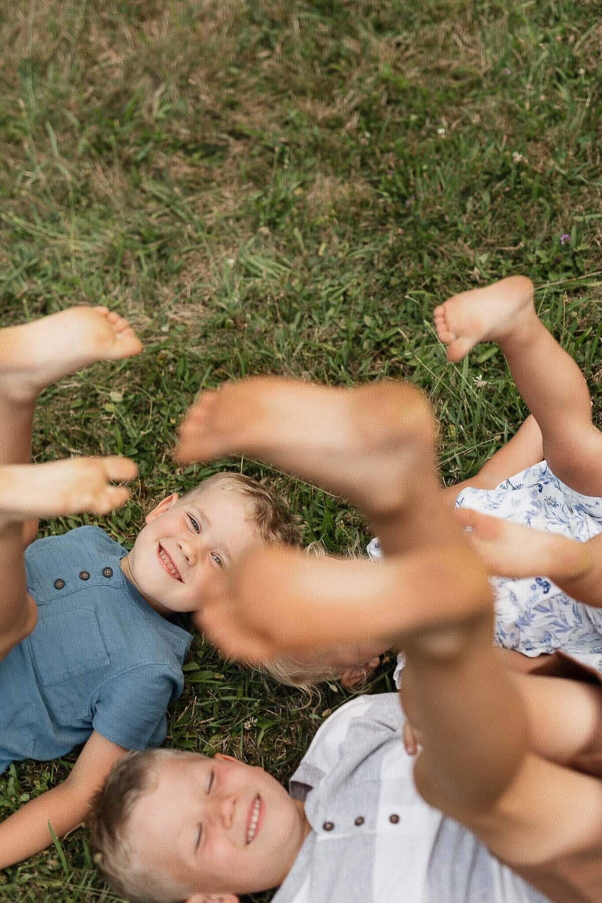 Three kids laying on grass with feet in the air during backyard family photography session.