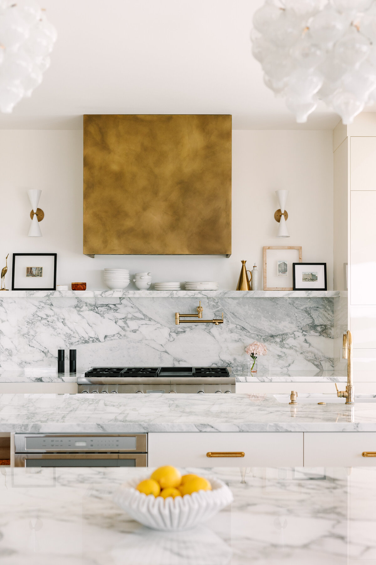 Kitchen with high gloss cream cabinets and Vagli marble counter and backsplash, brass range hood, and Thermador appliances.