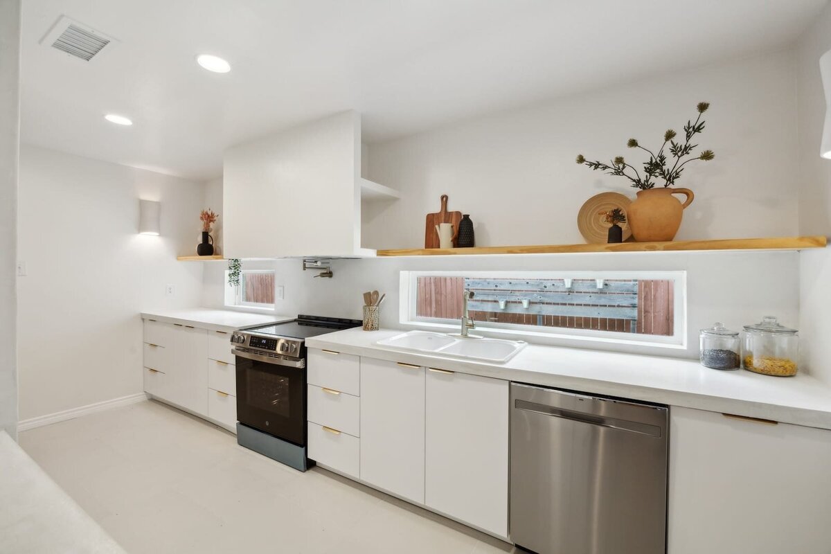 Bright modern kitchen at 3120 Chapel Downs Dr Dallas TX featuring white cabinetry, window shelf, stainless steel appliances, and minimalist decor — listed by Haven Realty Group.