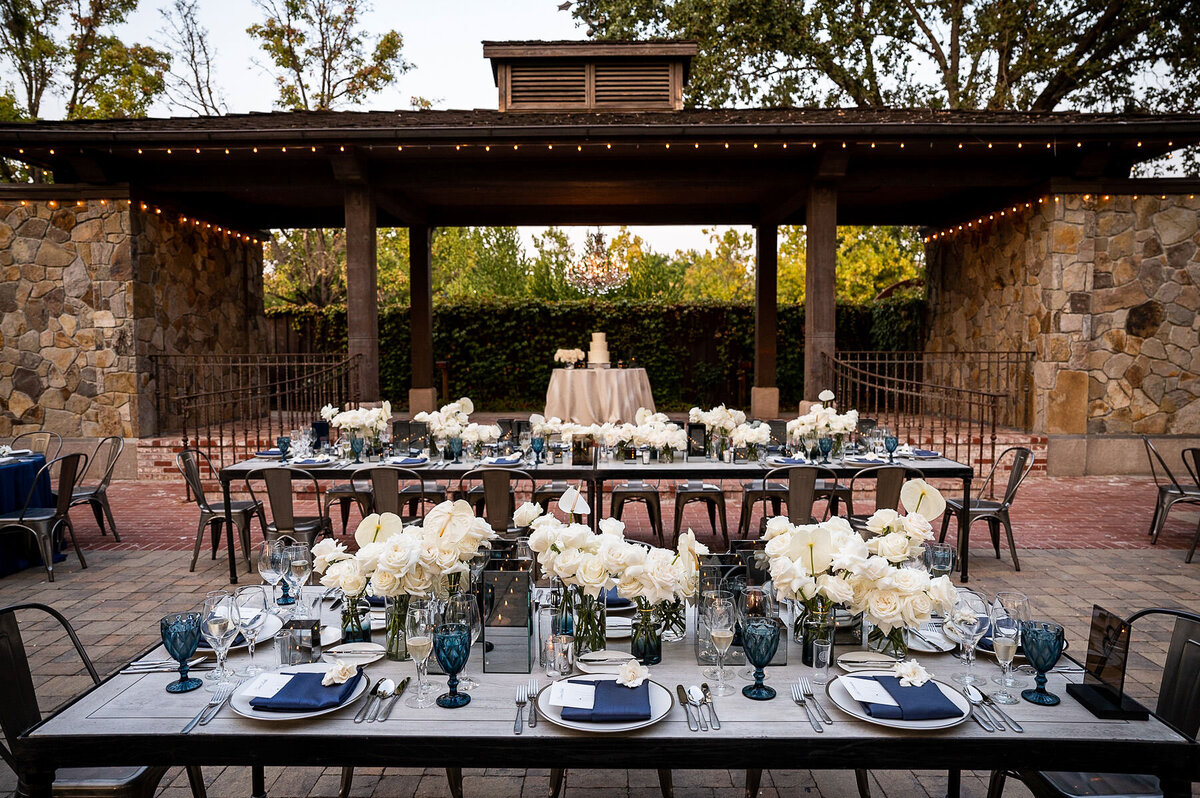 San Francisco Bay Area wedding photographer showcases elegant reception tablescape with white floral arrangements and navy accents under covered pavilion at Estate Yountville in Napa Valley